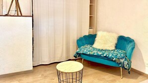 Une pièce avec un canapé de couleur turquoise, une table ronde et un rideau.