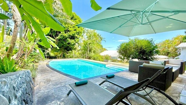 A swimming pool with lounge chairs and an umbrella, surrounded by tropical plants. - Le Refuge, Old Creole Villa with Swimming Pool (La Montagne)