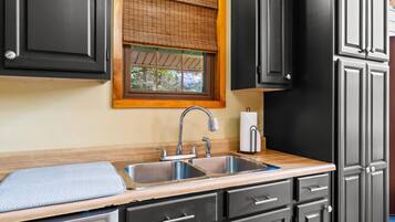 A kitchen with a stainless steel sink, black cabinets, a wooden countertop, and a window with blinds.