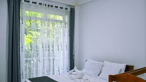 A clean, well-lit bedroom with a bed, curtains, and a view of greenery outside. - Eco Bless Inn (Kandy)
