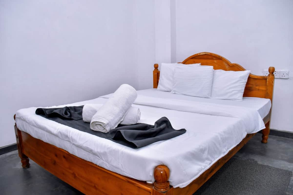 Una cama bien hecha con ropa de cama blanca y negra, un cabecero de madera y una pared blanca.