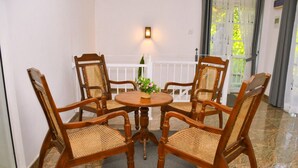 A round wooden table with four chairs, a small vase with flowers, and a wall-mounted light fixture. - Eco Bless Inn (Kandy)