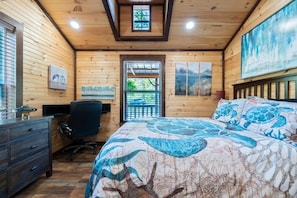 Une chambre dans une cabane en bois, avec un lit, un bureau, une chaise et des œuvres d’art accrochées aux murs.