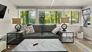 A modern living room with a grey sofa, two side tables with lamps, a coffee table, and large windows with blinds.