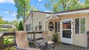 A wooden deck with two chairs and a small table, a covered porch, and a sign reading 'The Cottage.'