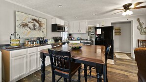 A kitchen with white cabinets, a wooden dining table, and a ceiling fan.