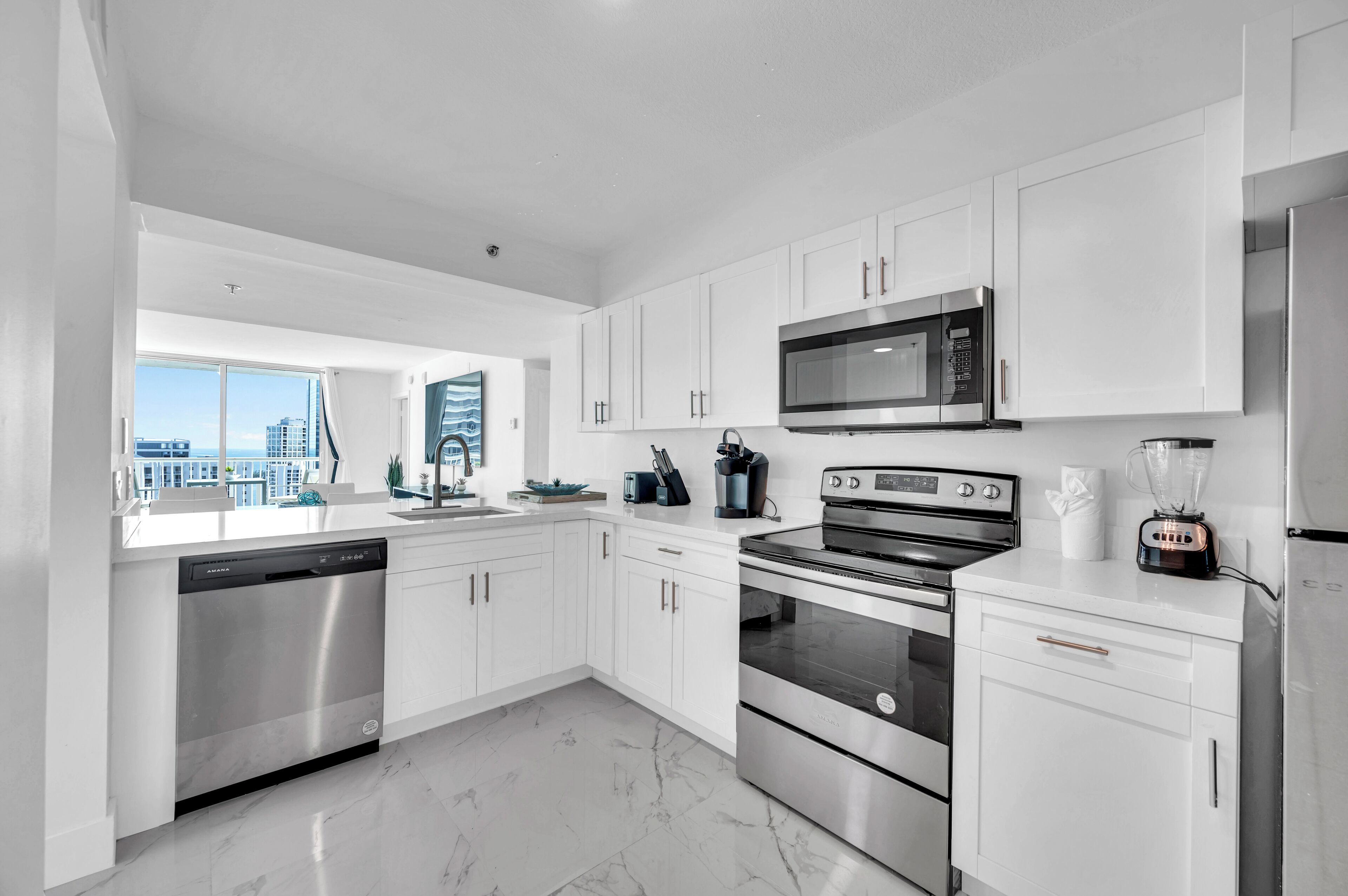 A modern kitchen with white cabinetry, stainless steel appliances, and a view of the city.