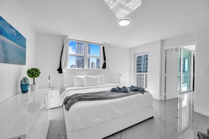 A modern bedroom with a large bed, a nightstand, a potted plant, and a view of the city through the window.