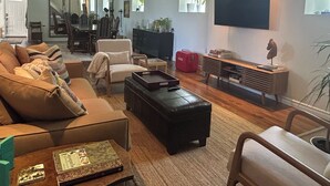 Uma sala de estar moderna com sofá, poltronas, mesa de centro, televisão e estante de livros.
