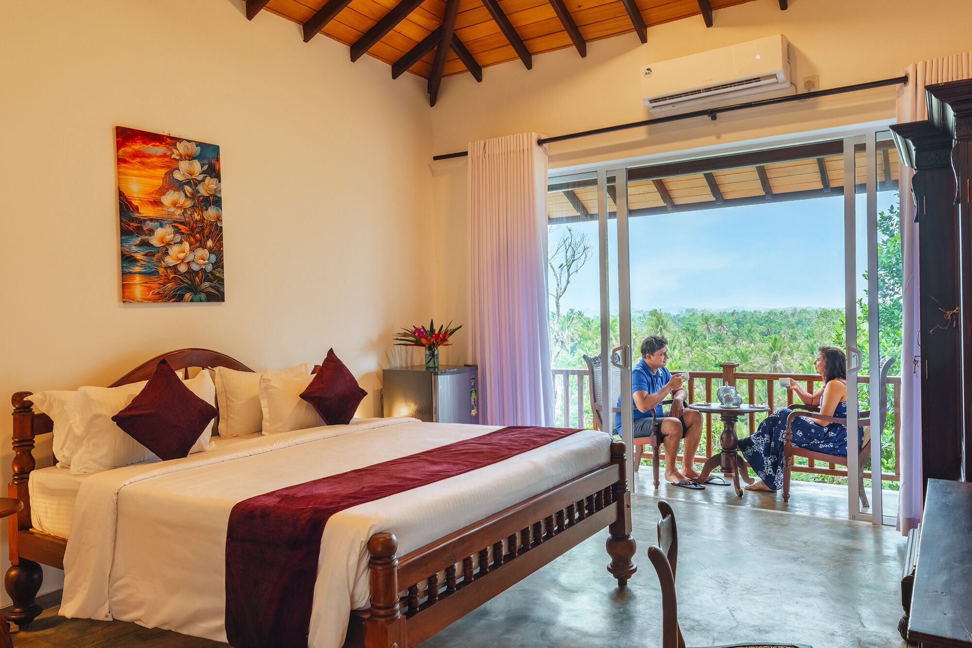 A bedroom with a large bed, a painting, and a balcony with a view.