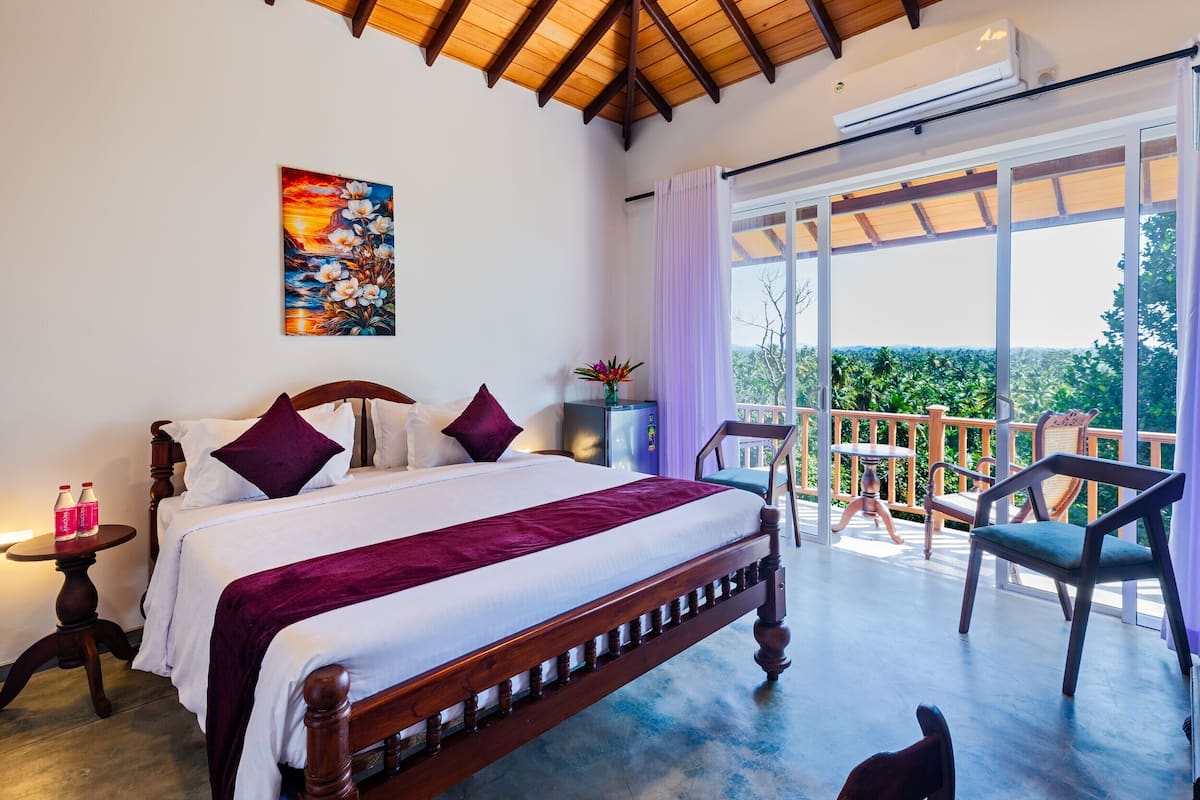 Un dormitorio con una cama grande, un cuadro en la pared, un balcón con una silla y vistas a la vegetación.