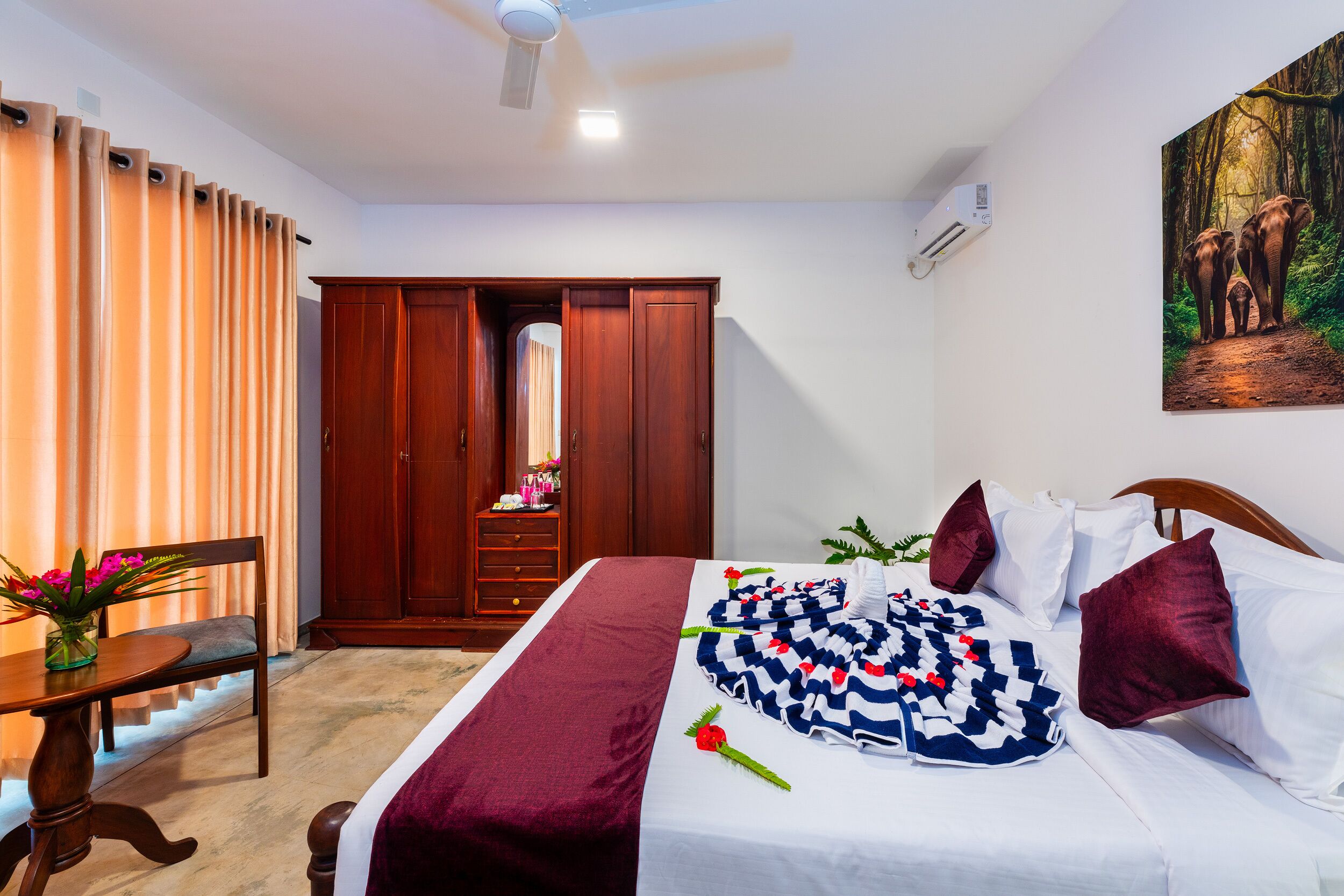 A hotel room with a bed, a wooden wardrobe, a desk with a chair, and a painting on the wall.
