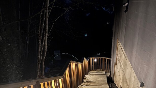 Una escalera con barandas de madera e iluminación que sube hacia un edificio.