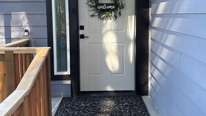 Una puerta principal con un cartel de 'welcome', una valla de madera y un pequeño jardín.
