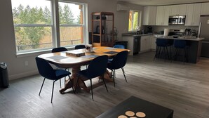 Una cocina moderna con armarios blancos, una isla central con taburetes y una zona de comedor con mesa de madera y sillas azules.