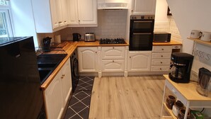 Ett modernt kök med vita skåp, en bänkskiva i trä, en inbyggd ugn, en mikrovågsugn och en kaffebryggare.