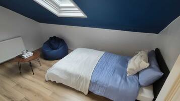 Un dormitorio con cama, sillón de plumas, una mesita y un tragaluz.