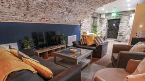 A cozy living room with a brick wall, a flat-screen TV, comfortable sofas, and a coffee table. - Gatehouse Studio Apartment (Castle Douglas)