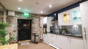 A modern kitchen with white cabinets, a black countertop, and a stone wall. - Gatehouse Studio Apartment (Castle Douglas)