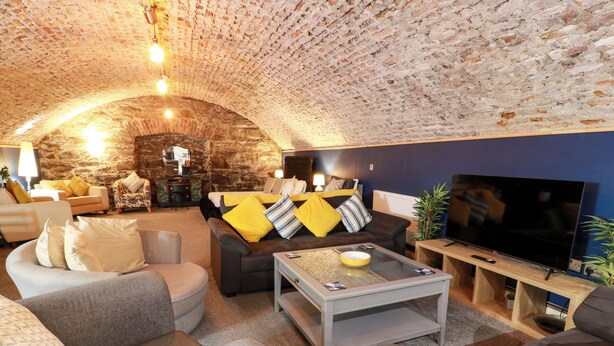 A cozy living room with a stone ceiling, a flat-screen TV, and comfortable seating. - Gatehouse Studio Apartment (Castle Douglas)