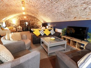 A cozy living room with a stone ceiling, a flat-screen TV, and comfortable seating. - Gatehouse Studio Apartment (Castle Douglas)