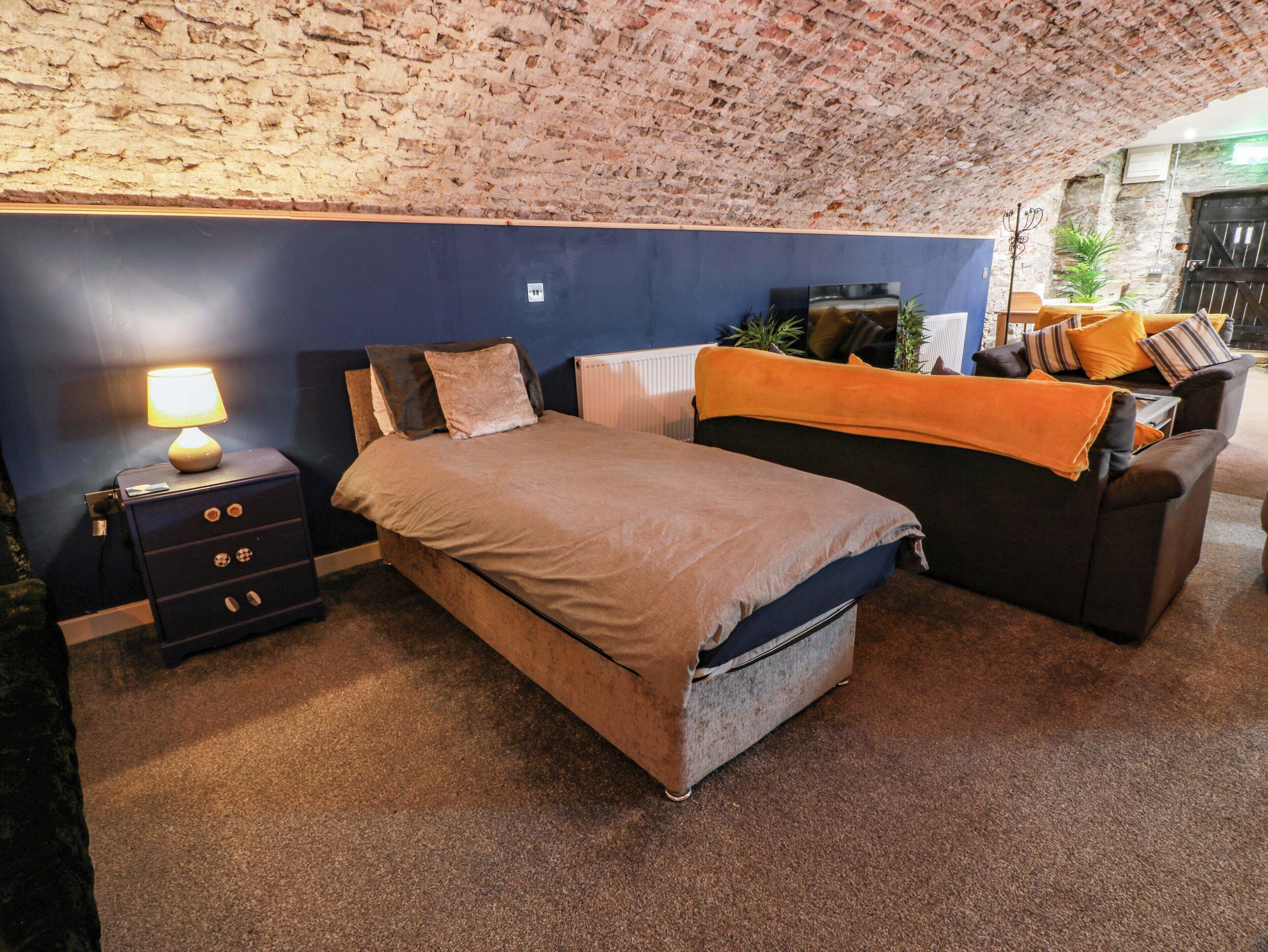 A bedroom with a bed, a nightstand, a dresser, a radiator, a sofa, and a brick wall.