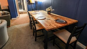 A dining area with a wooden table set for four, surrounded by chairs, in a room with blue walls and a brick ceiling. - Gatehouse Studio Apartment (Castle Douglas)