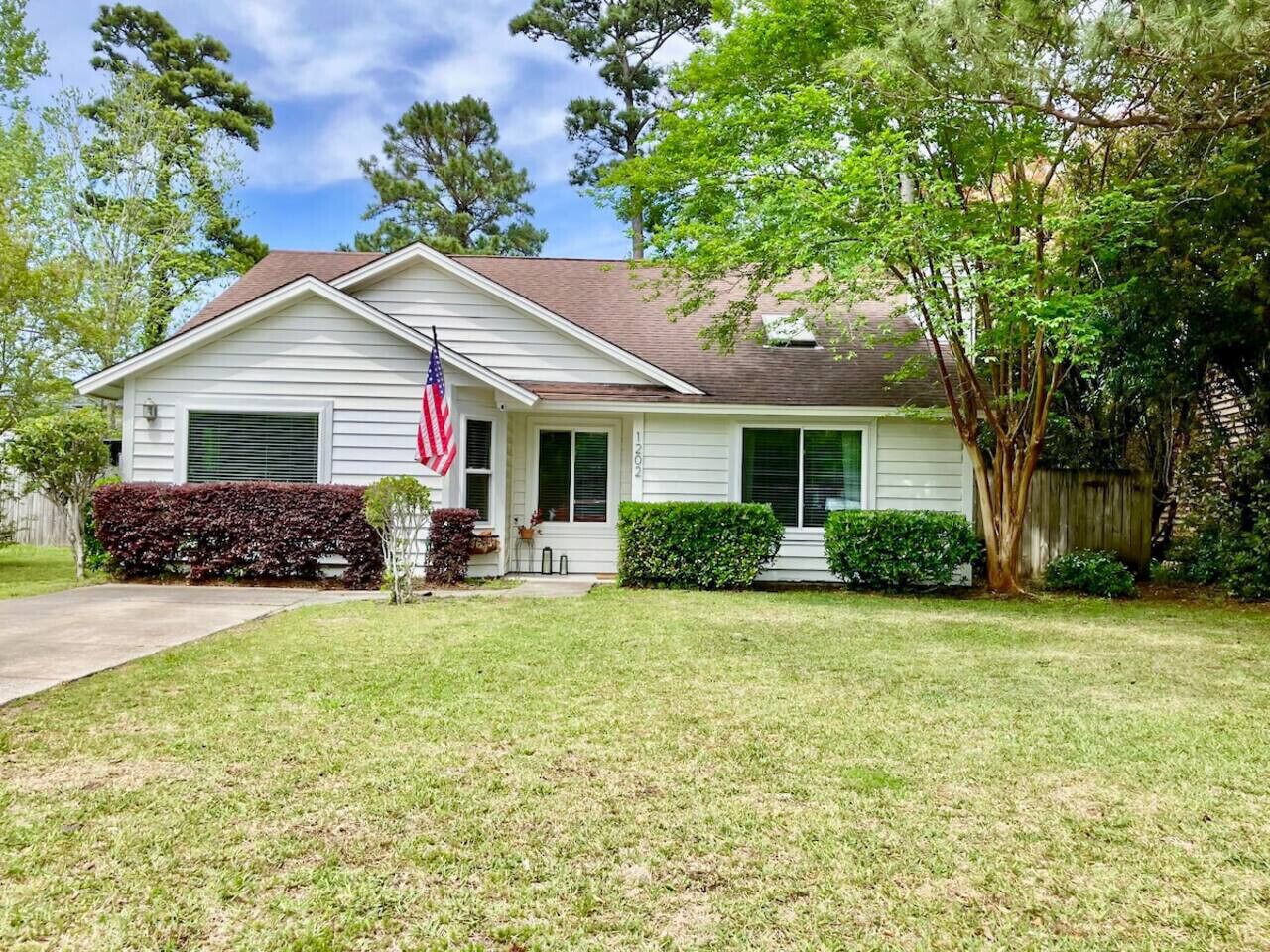 A single-story house with a front porch, a flag, and a well-maintained lawn.