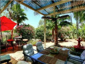 An outdoor patio area with a covered seating area, a table with a centerpiece, and various plants and trees. - 55+ Resort Living with Pool, Pickleball & Spa (Mesa)