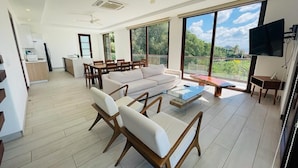A spacious living area with a sofa, chairs, a coffee table, and a TV. There is a balcony with a view of greenery. - Hacienda Iguana 3BR Corner Rooftop- Costamar (Tola)