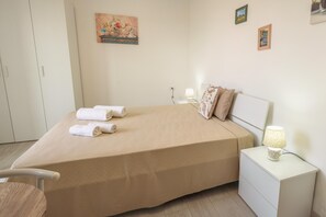 A neatly made bed with two rolled towels, a bedside lamp, and a small nightstand. - Appartamento Dei Tre Colli Rosa ... (Noto)