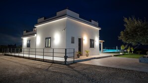 Una casa moderna de dos pisos con techo plano, ventanas grandes y exterior iluminado durante la noche.