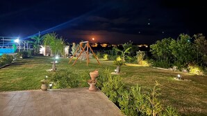 A nighttime outdoor area with a swing set, potted plants, and a well-lit pathway. - Appartamento Dei Tre Colli Blu -... (Noto)
