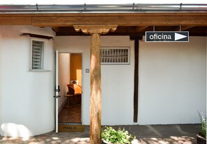 Entrada de un edificio con un porche de madera, un letrero que indica oficina, una puerta y un escalón pequeño que da acceso al interior.