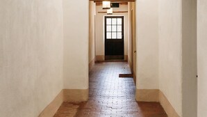 Käytävän lattia on tehty tiilistä, seinät ovat valkoiset ja katossa on kattotuuletin. Käytävän päässä on ovi, ja sen yläpuolella on valaisin.