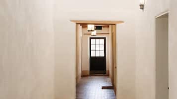 A hallway with a brick floor, white walls, and a ceiling fan. There is a door at the end of the hallway and a light fixture above it.