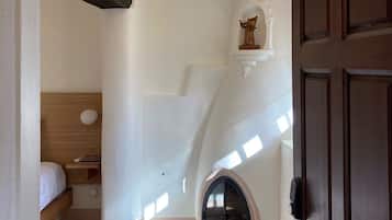 A narrow hallway with a wooden door, a small alcove with a bed, and a fireplace.