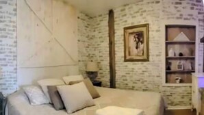 Une chambre à coucher avec un grand lit, une table de chevet, un mur orné d’un tableau encadré et une étagère avec divers objets.