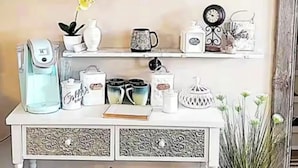 Une console blanche, ornée d ’objets décoratifs, avec une horloge et un panneau indiquant « CAFÉ » accroché au mur au-dessus.