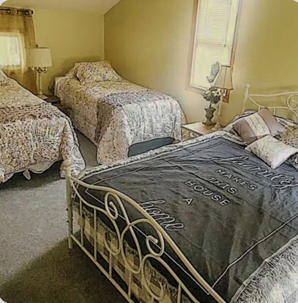 A bedroom with two single beds, a large bed, and a nightstand with a lamp.