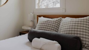 A neatly made bed with a gray and white checkered pillow, a white pillow, and a white towel on a white bedspread.