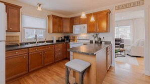 A modern kitchen with wooden cabinets, a central island, pendant lighting, and a view to the living area.