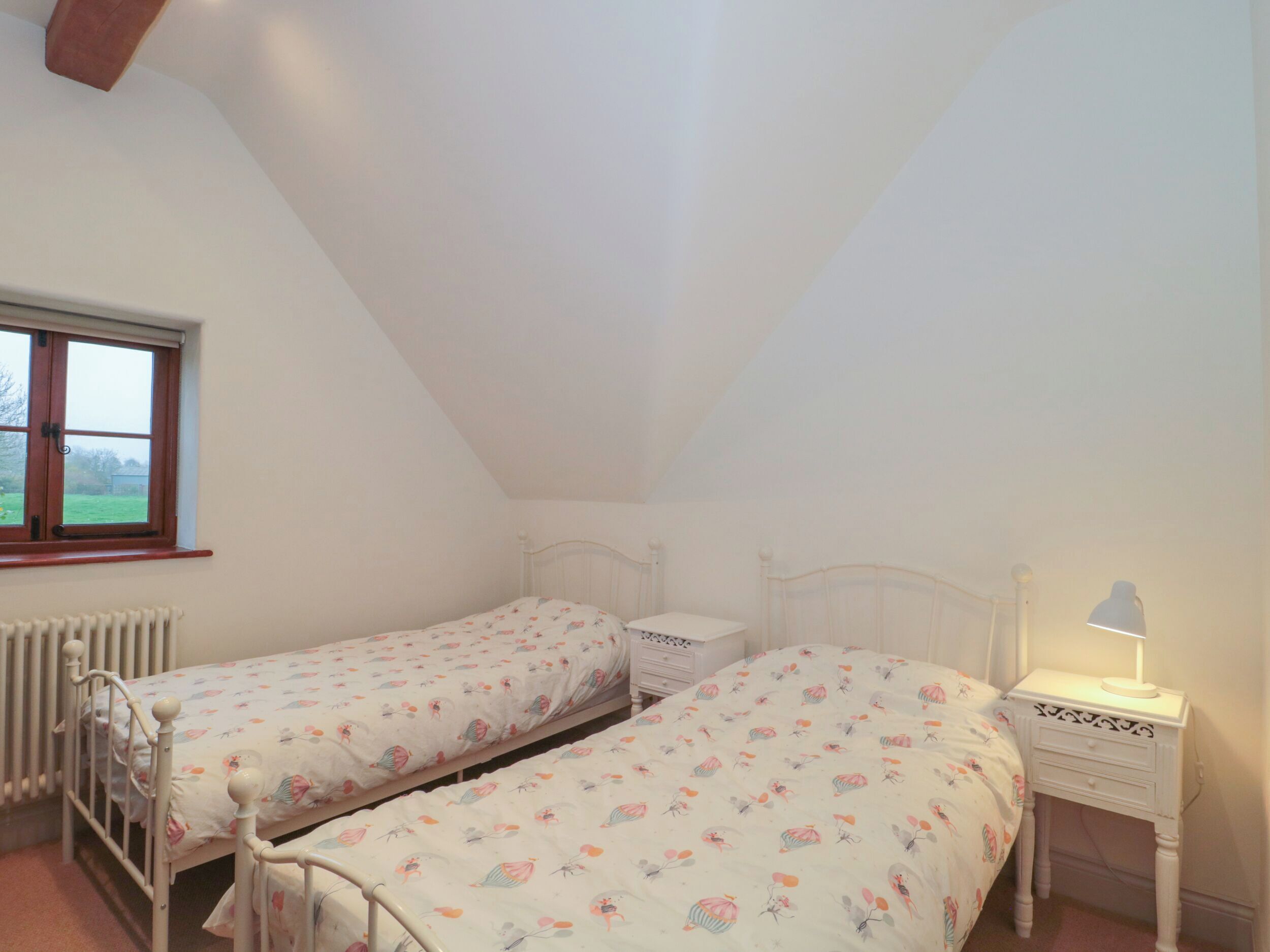 Ein Schlafzimmer mit zwei Einzelbetten, einem Fenster, einem Heizkörper und einem Nachttisch mit Lampe.