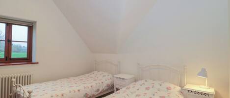 Ein Schlafzimmer mit zwei Einzelbetten, einem Fenster, einem Heizkörper und einem Nachttisch mit Lampe.