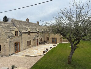 A stone building with multiple windows and doors, a paved courtyard, and a tree. - Manor Cottage (Bampton)