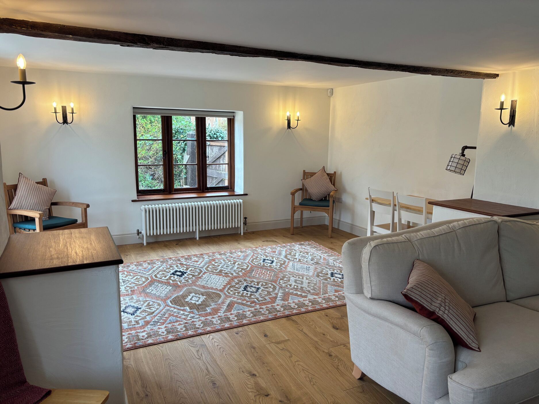 A cozy room with a radiator, a window with blinds, a patterned rug, and a sofa.