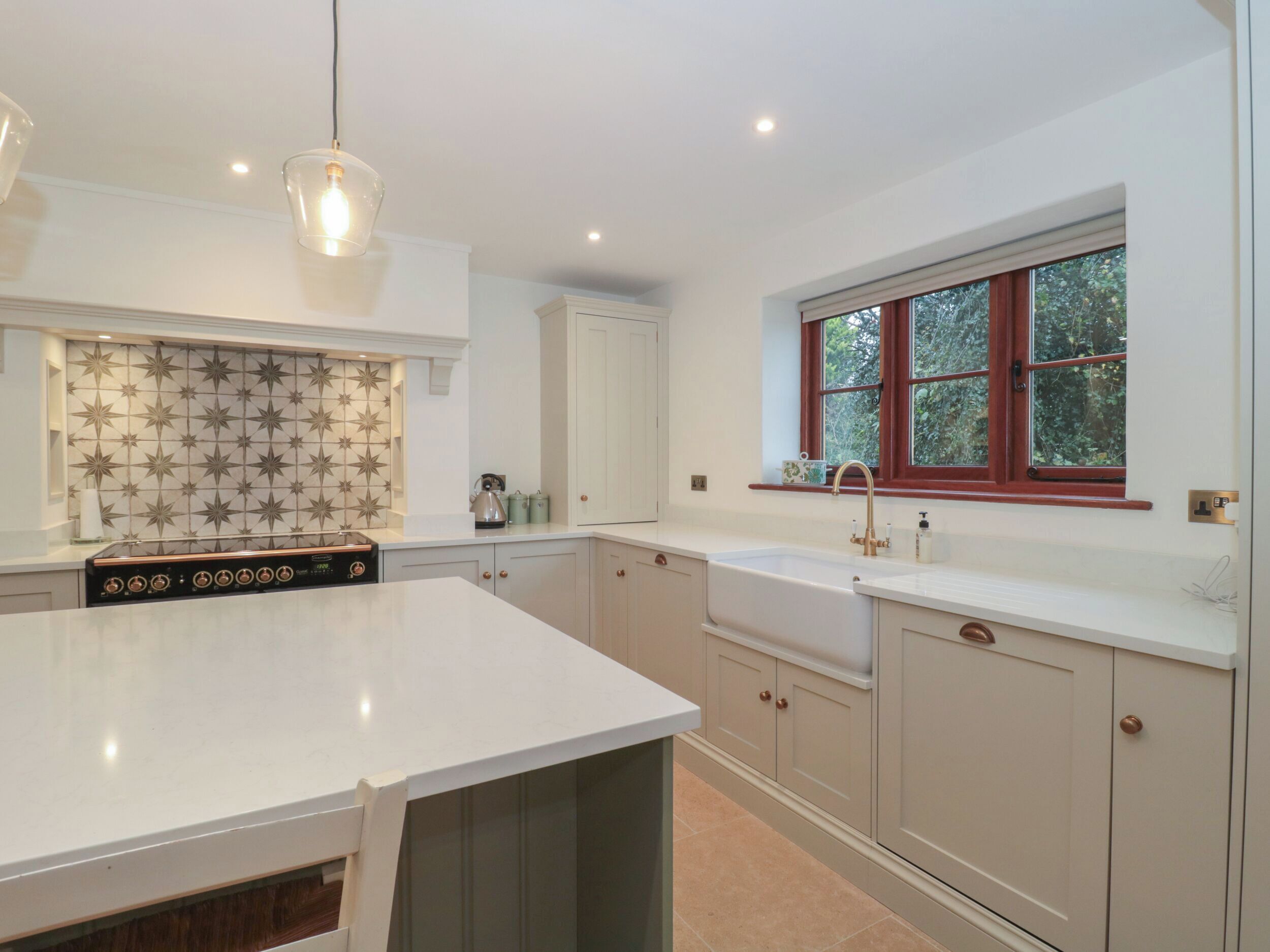 A modern kitchen with a large island, white cabinetry, and a window with a view of greenery.