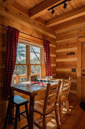 L’intérieur d’un chalet en bois, avec une table à manger, des chaises et une fenêtre ornée de rideaux à carreaux rouges et noirs.
