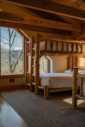 Une cabane en bois rustique, dotée d’un lit à l’étage et d’une grande fenêtre donnant sur une forêt.