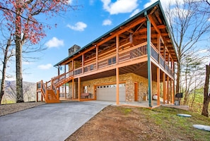 Une cabane en bois à deux étages, dotée d’un balcon, d’un garage et de fondations en pierre.